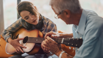 Adult learning to play an acoustic guitar with guidance from a music teacher