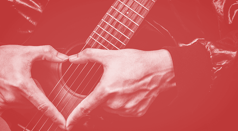 A musician forming a heart shape with their hands over an acoustic guitar, symbolizing love for music on Valentine’s Day.