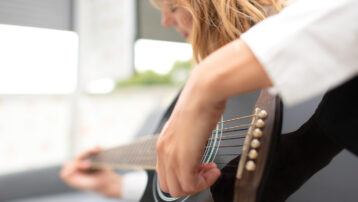 Close-up of a left-handed musician strumming a black acoustic guitar