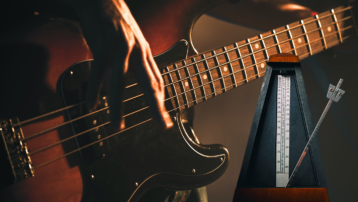 Close-up of electric bass guitar player practising precise timing with a mechanical metronome