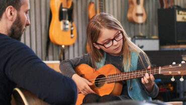 Child learning to play acoustic guitar with a music teacher – How to Choose Your First Instrument