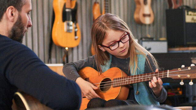 Child learning to play acoustic guitar with a music teacher – How to Choose Your First Instrument