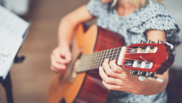 Child learning to play a small acoustic guitar, demonstrating correct guitar size for kids