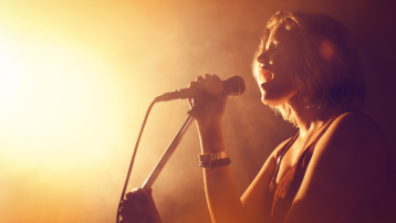 Female singer performing into a microphone on stage, illustrating 11 tips for a strong voice and better singing technique.