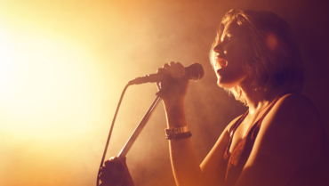 Female singer performing into a microphone on stage, illustrating 11 tips for a strong voice and better singing technique.