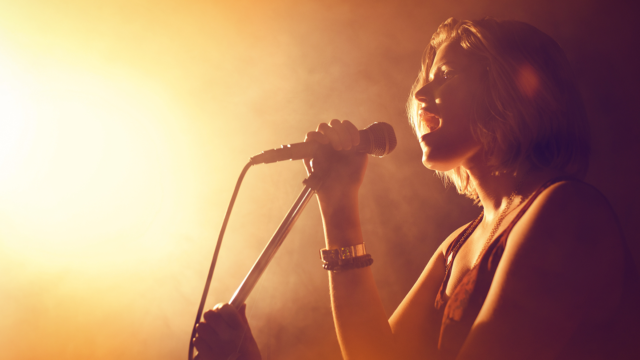 Female singer performing into a microphone on stage, illustrating 11 tips for a strong voice and better singing technique.