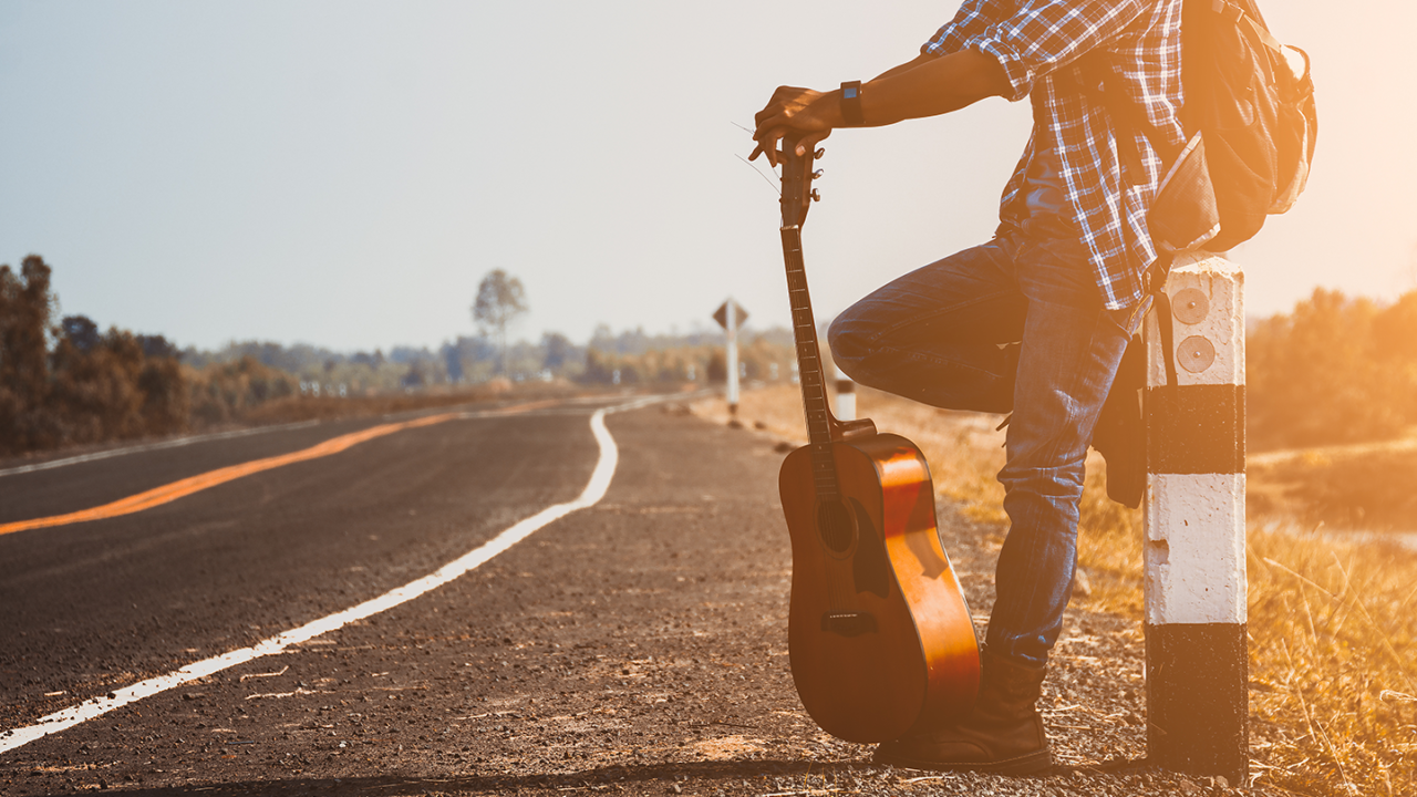Musician standing beside a road with a travel guitar, ready for a vacation and outdoor music adventure.