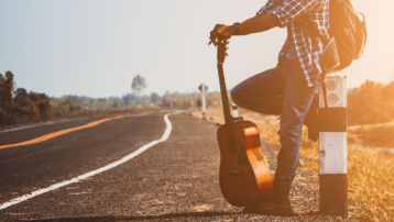 Musician standing beside a road with a travel guitar, ready for a vacation and outdoor music adventure.