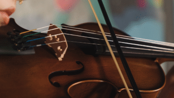 Close-up of a violin being played with a bow, highlighting the strings and wooden body, used to illustrate the difference between a violin and a viola