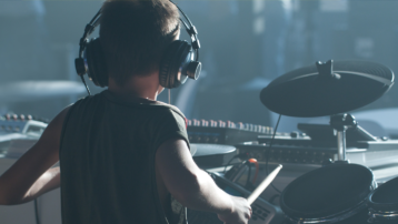 Young beginner drummer wearing headphones while practicing on an electronic drum kit and learning basic drumming techniques.