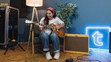Guitarist smiling while playing a Les Paul electric guitar in front of a Fender amp in a music room: Beginner’s Guide to Guitar Amps