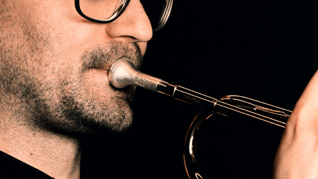Man playing a trumpet with focused breathing technique, close-up of mouthpiece and facial muscles.