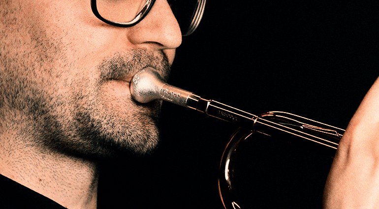 Man playing a trumpet with focused breathing technique, close-up of mouthpiece and facial muscles.