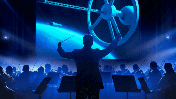 Conductor and orchestra performing with a space station visual, referencing The Blue Danube scene from 2001: A Space Odyssey
