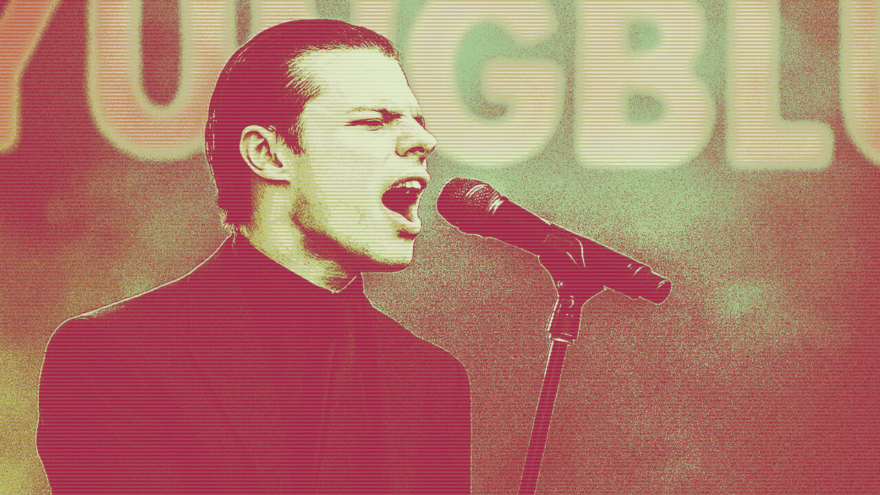 Yungblud singing into a microphone during a live performance with “YUNGBLUD” lit up in the background