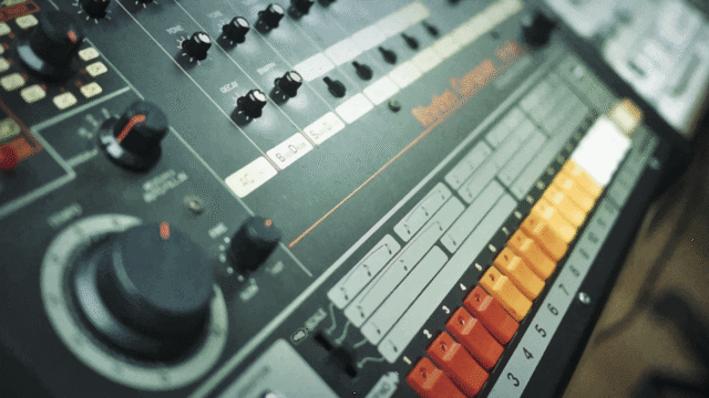 808 day: Close-up view of Roland TR-808 drum machine featuring colorful step-sequencer buttons and analog controls.