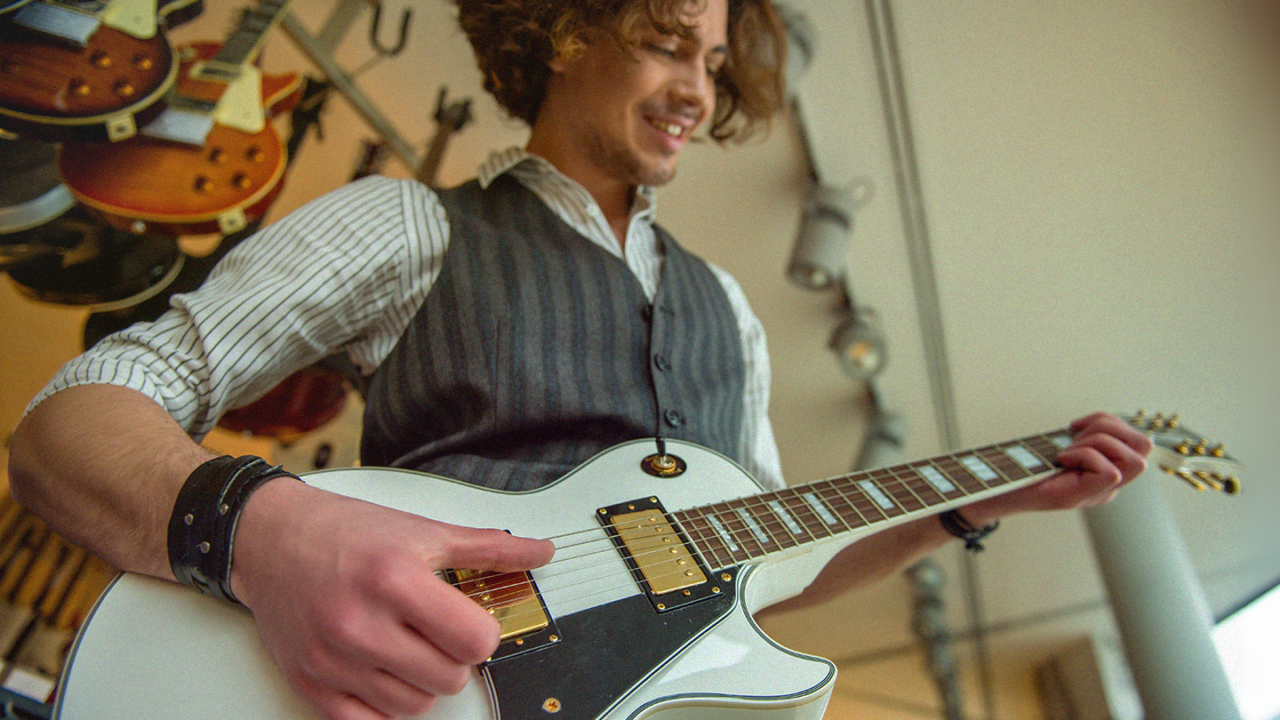 Beginner guitarist playing a white electric guitar in a guitar shop