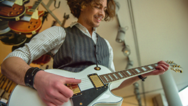 Beginner guitarist playing a white electric guitar in a guitar shop