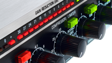Close-up of audio compressor knobs and gain reduction meter on studio hardware unit.