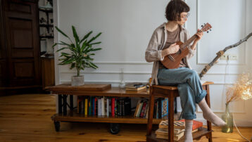 Person playing ukulele at home – benefits of learning a musical instrument