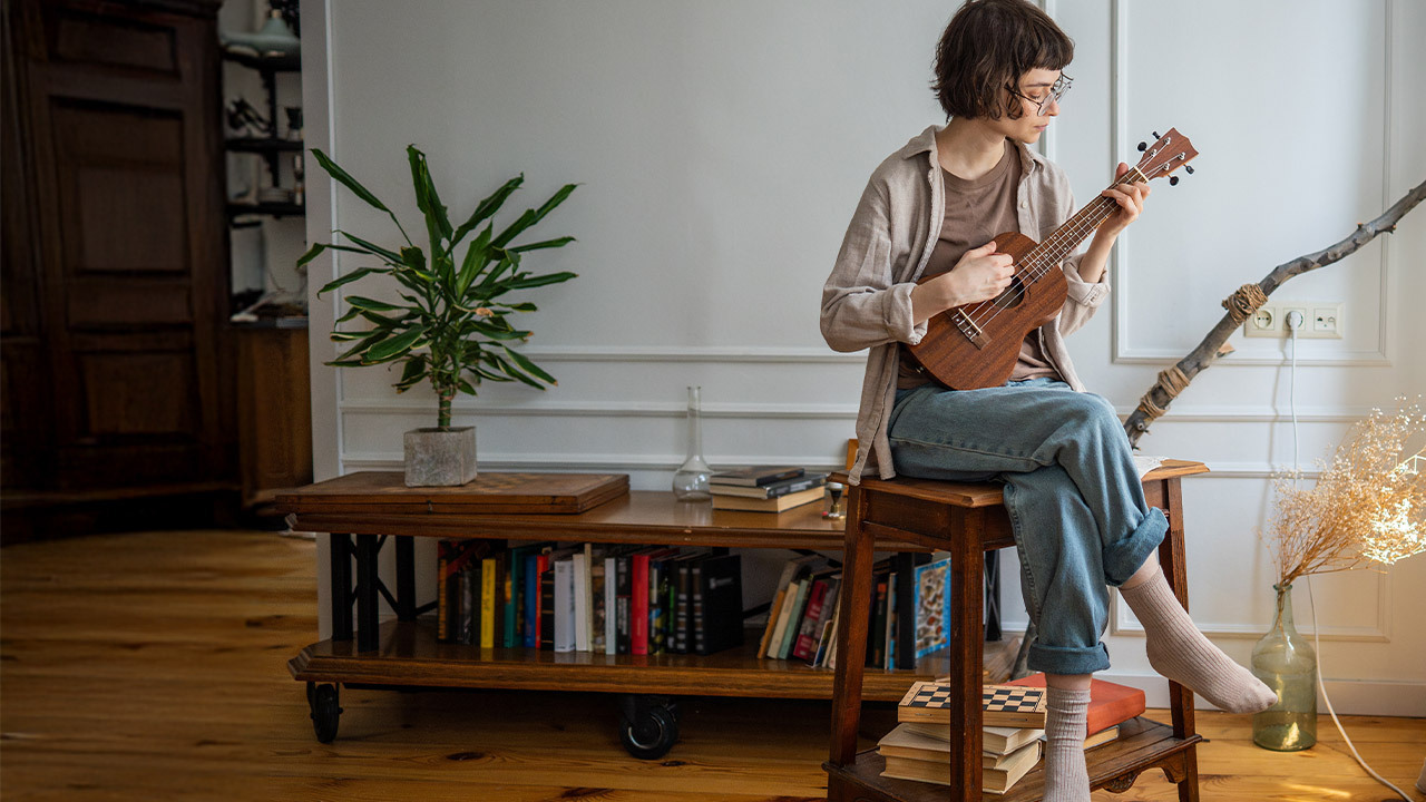 Person playing ukulele at home – benefits of learning a musical instrument
