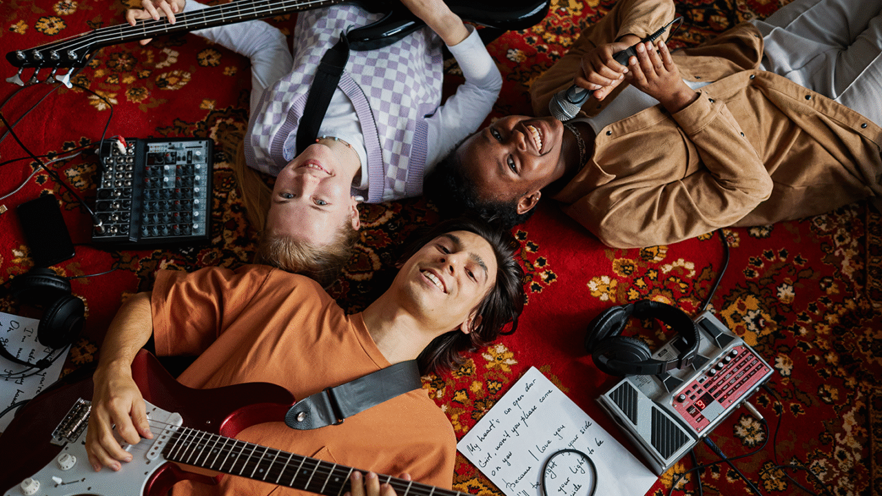 Group of young amateur musicians lying on a carpet with guitars, bass, microphone, and pedals, enjoying music together – Why being an amateur musician is "still" amazing