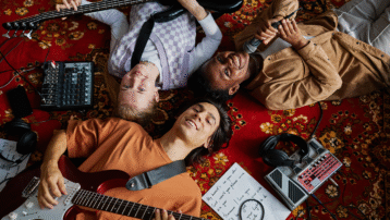 Group of young amateur musicians lying on a carpet with guitars, bass, microphone, and pedals, enjoying music together – Why being an amateur musician is "still" amazing