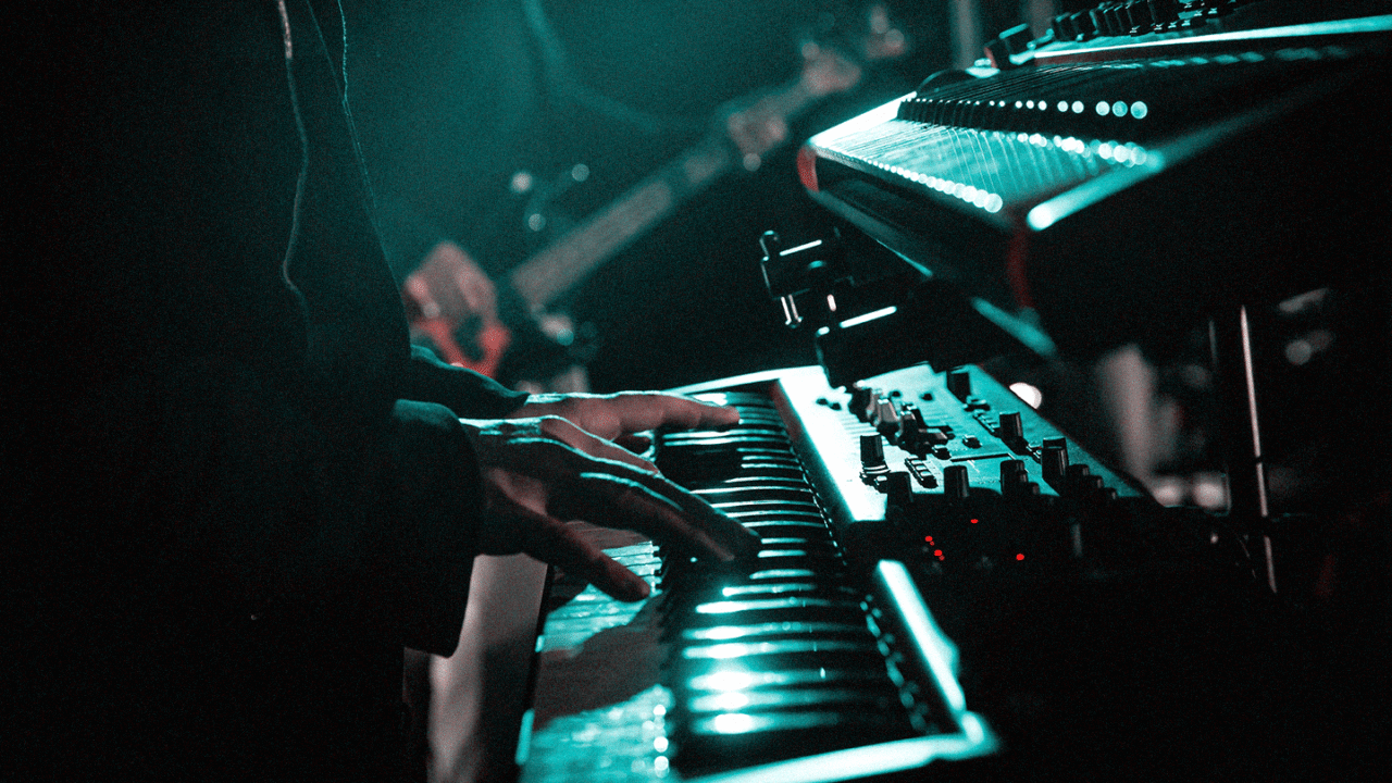 Using Keyboards Live: From Stands to Cabling :Close-up of a musician playing a keyboard on stage with synthesizer equipment and stage lighting.