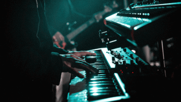Using Keyboards Live: From Stands to Cabling :Close-up of a musician playing a keyboard on stage with synthesizer equipment and stage lighting.