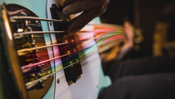 Close-up of a bassist plucking electric bass strings with colorful light streaks