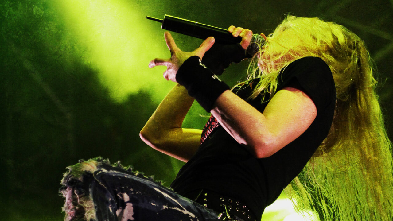 Female metal singer performing live on stage with microphone and dramatic lighting during a heavy metal concert
