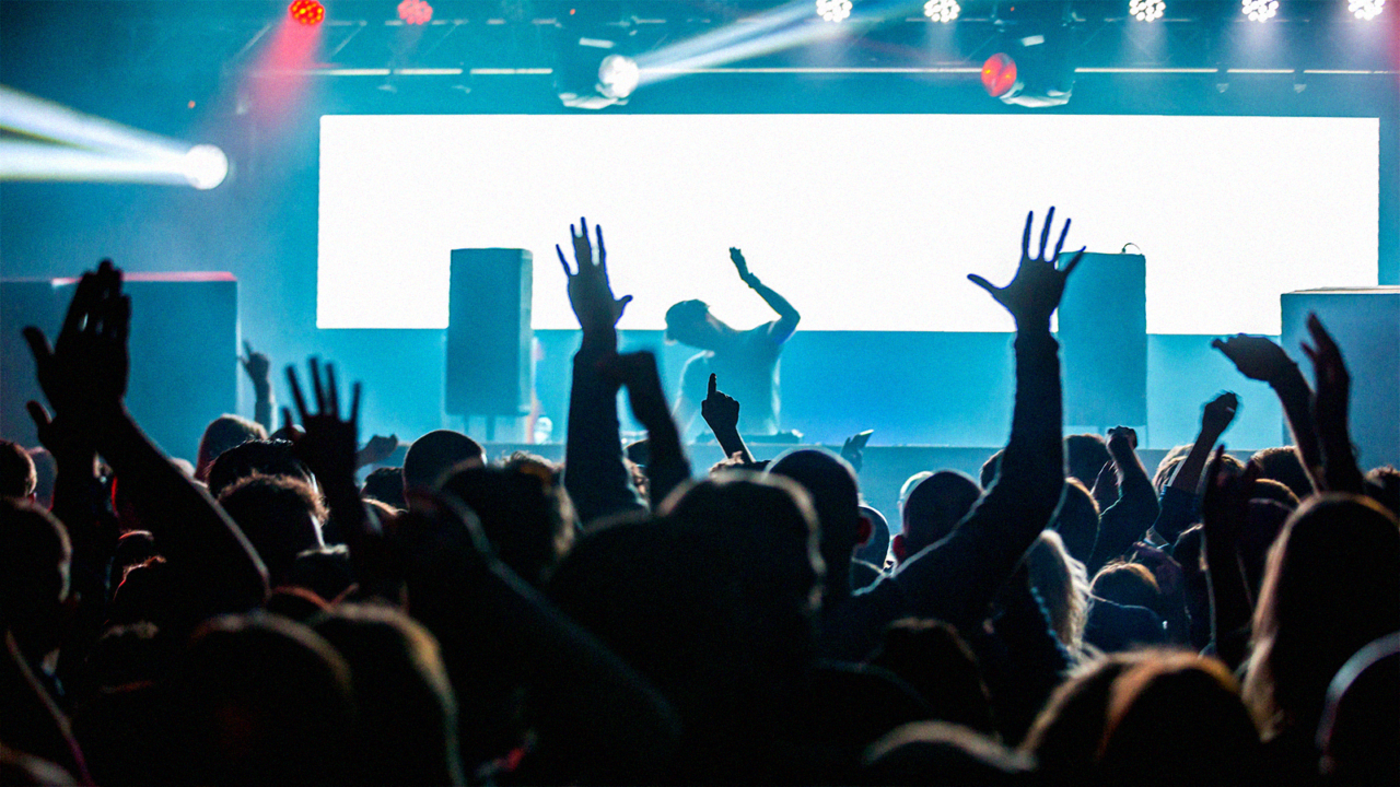 DJ performing live in a club while crowd raises hands and reacts on a packed dancefloor