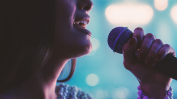 Close-up of a woman singing into a microphone on stage, illustrating the human voice as a unique musical instrument