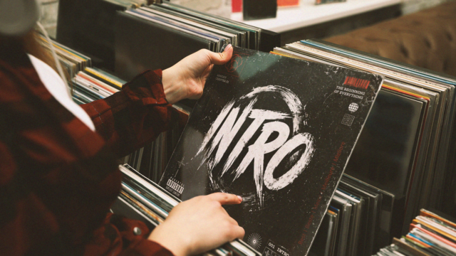 Person browsing vinyl records while holding a record sleeve reading "Intro", representing the best and most iconic song intros in music history.