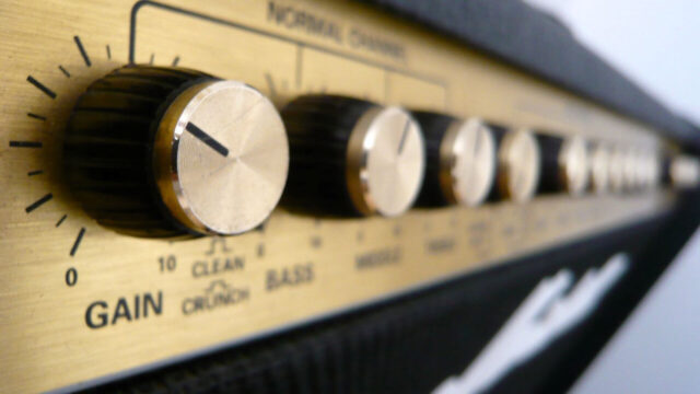 Close-up of the control knobs on a guitar amplifier, showing gain and EQ settings for a beginner guitar amp.