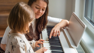Adult teaching a child to play the keyboard at home