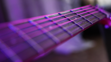 Close-up of acoustic guitar strings along a fretboard under purple lighting.
