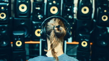 Person wearing headphones in front of a wall of studio speakers, illustrating the choice between studio monitors and headphones for music production.